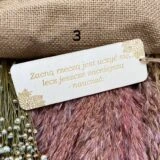 Pojedyncza drewniana zakładka do książki z jasnego drewna z grawerowanym cytatem: "Zacną rzeczą jest uczyć się, lecz jeszcze zacniejszą nauczać". Na górze przewiązany surowy sznurek jutowy.