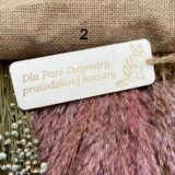 Drewniana zakładka do książki z jasnej sklejki z grawerem wykonanym ozdobną czcionką: "dla Pani Dagmary prawdziwej kociary". Na górze przewiązany naturalny sznurek jutowy.